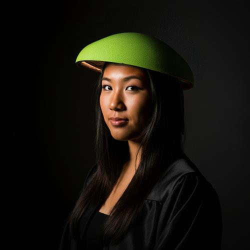A portrait-style, AI-generated image of a young woman in graduation gown wearing a hardhat that looks like a lime slice on her head.